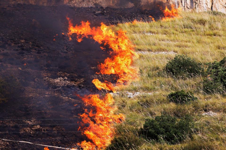 Flames burn in a field in Capaci, near Palermo, in Sicily, southern Italy, Wednesday, July 26, 2023. On the island of Sicily, two people were found dead Tuesday in a home burned by a wildfire that temporarily shut down Palermo's international airport, according to Italian news reports. Regional officials said 55 fires were active on Sicily, amid temperatures in the 40s Celsius. (Alberto Lo Bianco/LaPresse via AP)