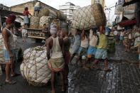 FILE - In this Aug. 21, 2013, file photo, Indian laborers carry a giant basket of vegetables to a wholesale market in Kolkata, India. In a report released Wednesday, Sept. 25, 2019, the Asian Development Bank says that escalating trade tensions will sap Asian economies of some of their potential in this year and the next. (AP Photo/Bikas Das, File)