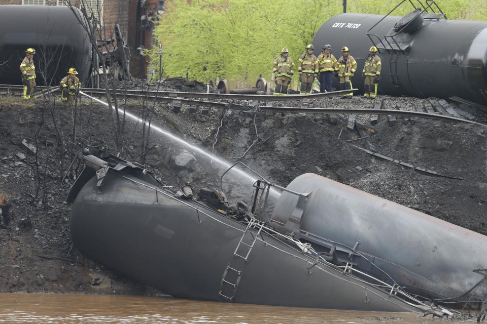 Firefighters and rescue workers work along the tracks where several CSX tanker cars carrying crude oil derailed and caught fire along the James River near downtown in Lynchburg, Va., Wednesday, April 30, 2014. Police said that 13 or 14 tanker cars were involved in the derailment. (AP Photo/Steve Helber)