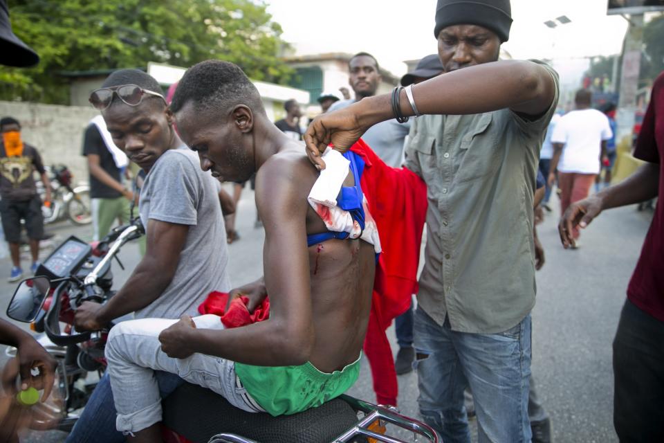 A wounded man is evacuated on a motorcycle during clashes to demand the resignation of Haiti's president Jovenel Moise on the 216th anniversary of Battle of Vertieres in Port-au-Prince, Haiti, Monday, Nov. 18, 2019. At least four people were shot and wounded during a small protest in Haiti’s capital after a speech by embattled President Jovenel Moise. A local journalist, a police officer and two protesters were rushed away with apparent bullet wounds. (AP Photo/Dieu Nalio Chery)