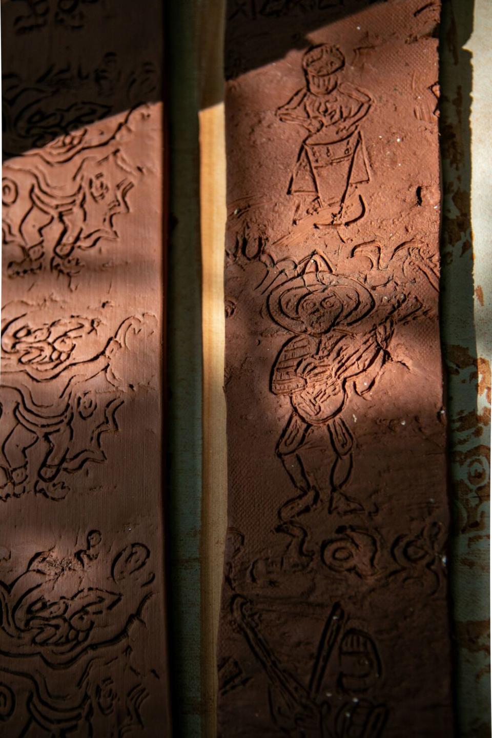 Detail of clay strips with line drawings of characters carved into them.