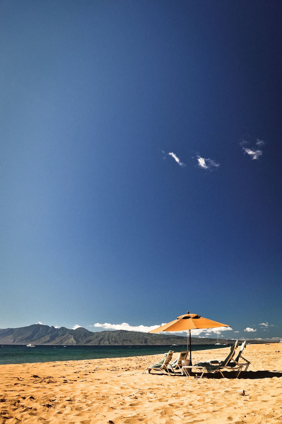 chairs and umbrella on beach with mountains in the background