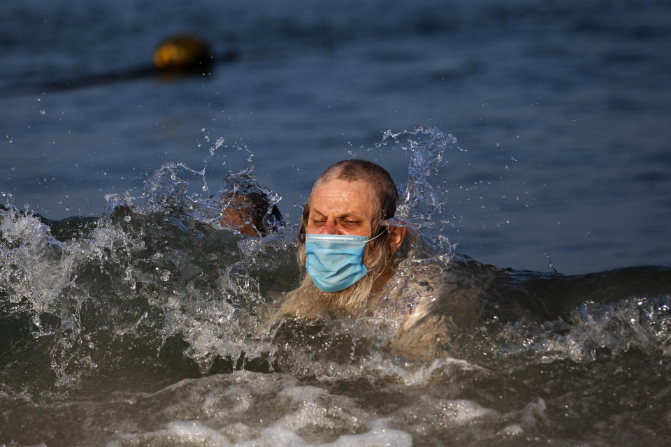 An ultra-orthodox Jewish man wears a protective face mask swims in the sea on a segregated beach in Tel Aviv, Israel, Wednesday, July 8, 2020. (AP Photo/Oded Balilty)
