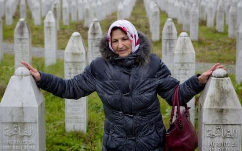 A woman touches grave stones at the memorial center of Potocari near Srebrenica - Credit: Amel Emric/AP