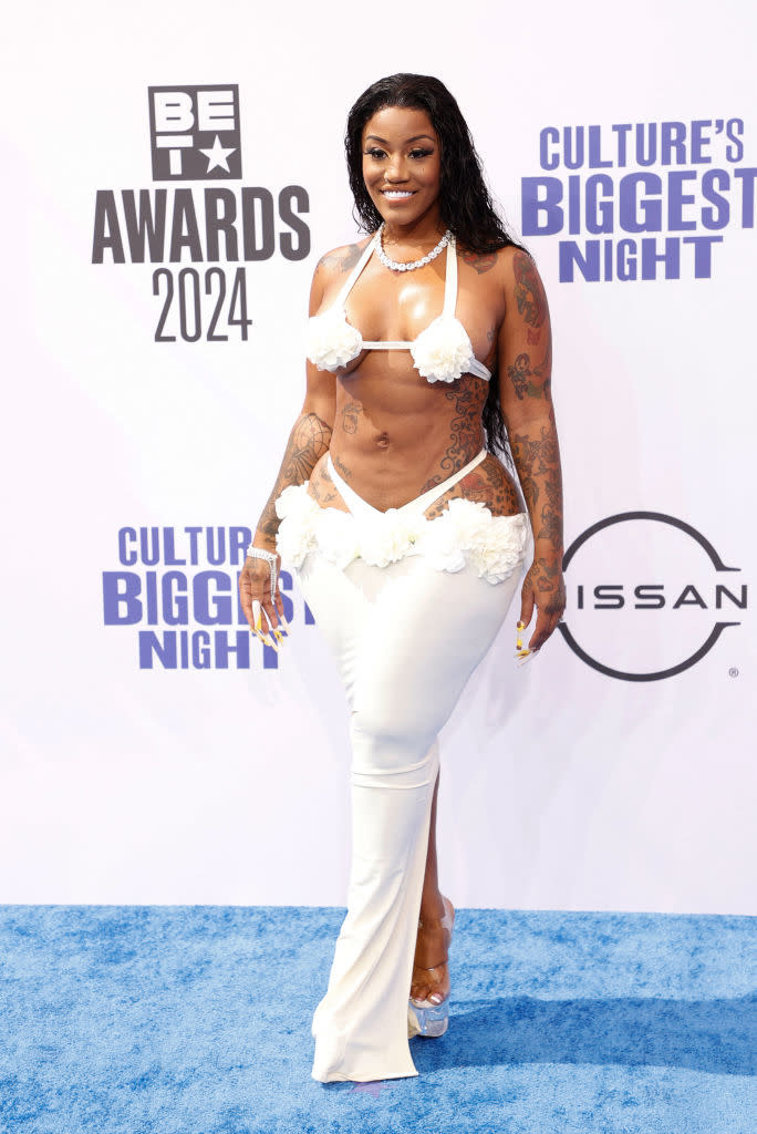 Jhonni Blaze on the BET Awards 2024 red carpet wearing a white, revealing two-piece outfit with floral details, smiling and posing for photos