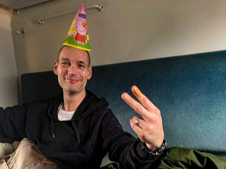 A man holds up the peace sign while wearing a party hat.