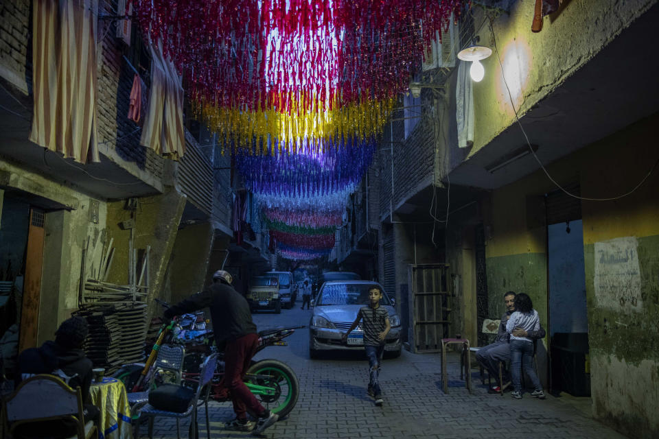 People sit under decorations hung up for Ramadan a day ahead of the holy month, in the Imbaba neighborhood of Giza, April 23, 2020. Muslims around the world are trying to maintain the cherished rituals of Islam holiest month during the coronavirus pandemic. (AP Photo/Nariman El-Mofty)