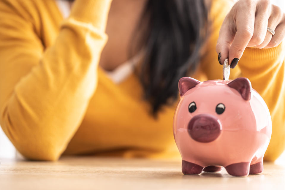 A person in a yellow top is putting a coin into a pink piggy bank