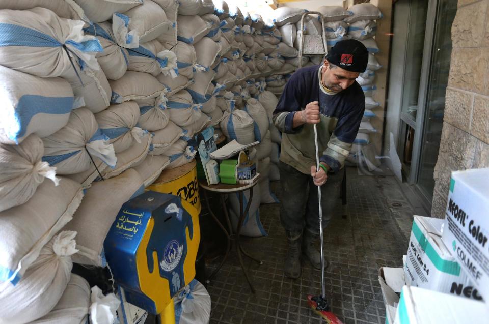 A Lebanese worker cleans next to sand barriers that were set in front of a shop, in a Shiite neighborhood of a southern suburb of Beirut, Lebanon, Tuesday, Jan. 28, 2014. After a wave of car bomb attacks on Hezbollah's stronghold south of Beirut that left scores of people dead or wounded over the past three months, shop owners scared of more bombs have set up sand barriers in front of their institutions to reduce damage in case more blasts occur. The attacks that hit the south Beirut area known as Dahiyeh (suburb) has sacred many people in the area and increased security measures by Lebanese troops and members of the militant group.(AP Photo/Hussein Malla)