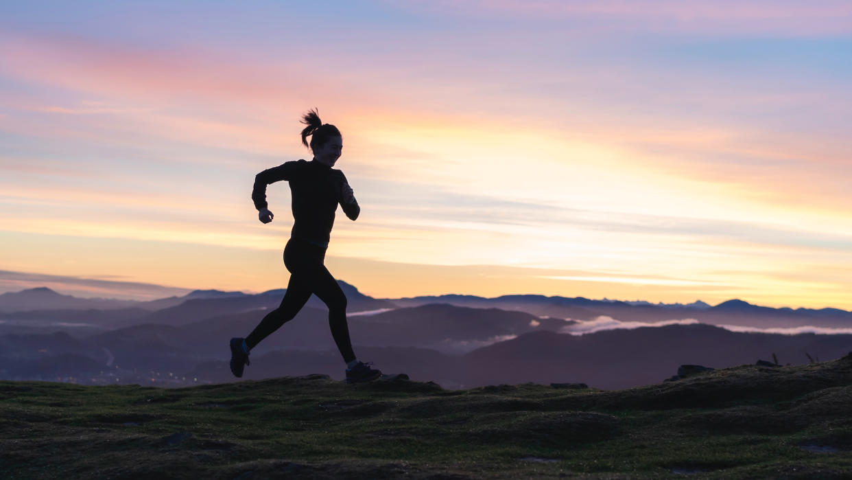  Woman running on hill at sunrise. 