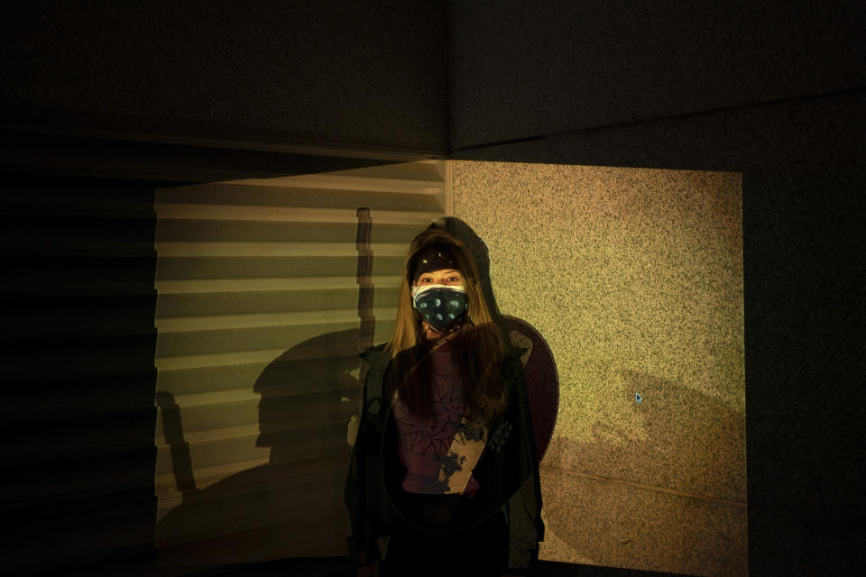 A protester who identified herself as Cindy, poses for a portrait as a projector displays a photograph, previously taken during the unrest, over her at a protest in Hong Kong. An attempt last month to impose a city-wide mask ban only further inflamed the demonstrators, who now cover up in defiance. "Wearing a mask right now is a statement against the Emergency Law," Cindy said. (Photo: Felipe Dana/AP)