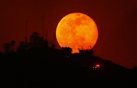 An emergency vehicle makes is way past a rising moon as it travels along a burned-out hillside near San Marcos, California May 14, 2014.REUTERS/Mike Blake