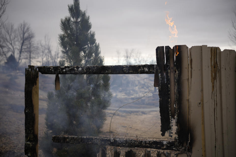 Flames leap from a fence near the remains of homes burned by wildfires after they ripped through a development, Friday, Dec. 31, 2021, in Superior, Colo. Tens of thousands of Coloradans were driven from their neighborhoods by wind-whipped wildfires. (AP Photo/David Zalubowski)