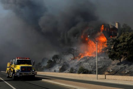 A fire crew passes a burning home during a wind-driven wildfire in Ventura. REUTERS/Mike Blake