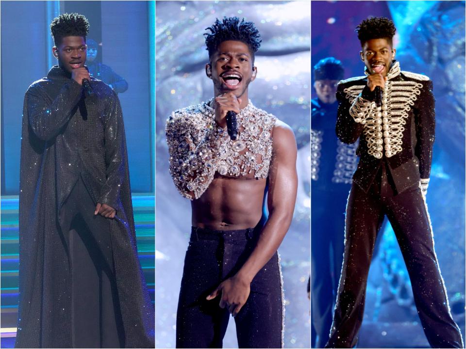 Lil Nas X in a black sparkling floor-length cape and matching trousers. In one look he wears a one-armed crystal crop top and black sparkling trousers. In another he's wearing a sparkling black marching band costume.