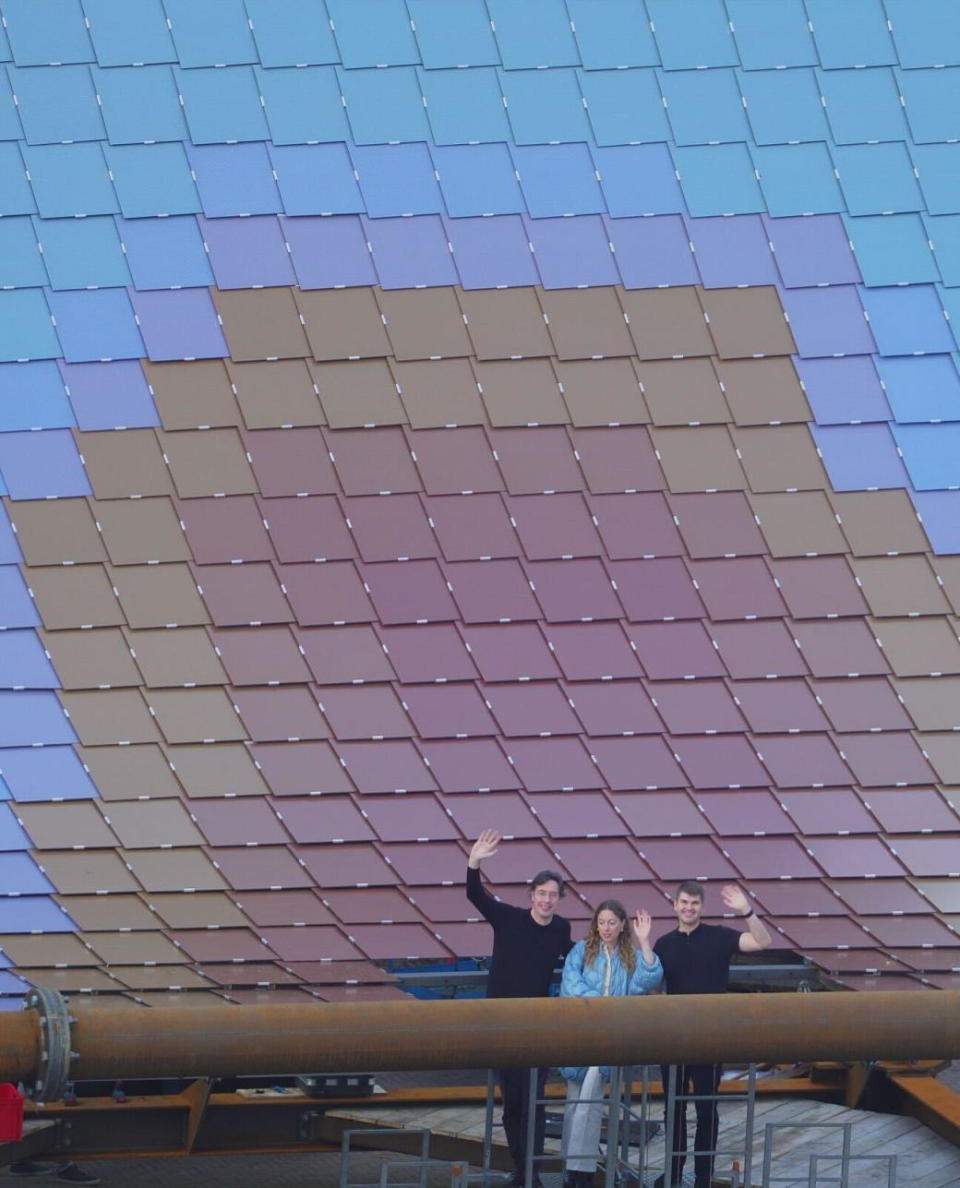 Marjan van Aubel and the V8 Architects founders smile and wave in front of their colorful solar pavilion at Dutch Design Week 2022.