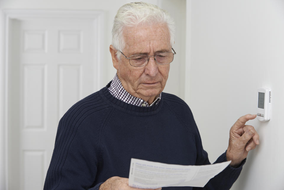 Worried Senior Man With Bill Turning Down Central Heating Thermostat interest rates.