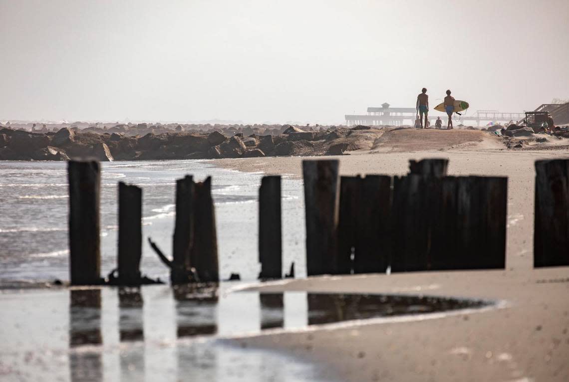 Surfers cross a rock goin at Folly Beach where old wooden groins are deteriorating. Shifting sands are having opposite effects on some Charleston area beaches with erosion claiming the Folly Beach shoreline while Sullivan Island’s beach is growing. July 21, 2022.