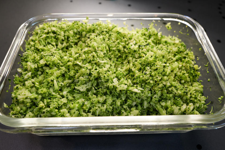 Chopped green herbs in a clear glass dish on a dark surface