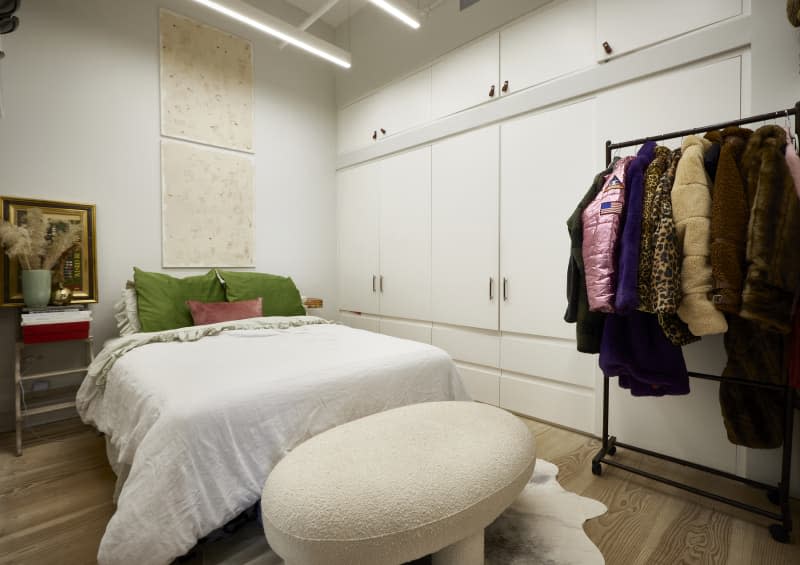 Neatly made bed in white room with closet lined wall.