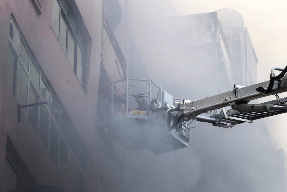 Firefighters attempt to rescue a man with a ladder from a market building during a fire at China town Thursday, Feb. 20, 2020, in Yangon, Myanmar. Firefighters contained a blaze in the 12-story building in the country's biggest city, Yangon. (AP Photo/Thein Zaw)