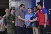 In this Jan. 23, 2020, photo provided by the Malacanang Presidential Photographers Division, Philippine President Rodrigo Duterte, center, is greeted by Social Welfare and Development Secretary Rolando Bautista, right, at the San Isidro Central School during the distribution of benefits to former rebels in Leyte province, southern Philippines. Duterte has renewed a threat to terminate an accord that allows American forces to train in the country unless Washington restored a visa of a political ally linked to human rights violations. (Karl Norman Alonzo/Malacanang Presidential Photographers Division via AP)