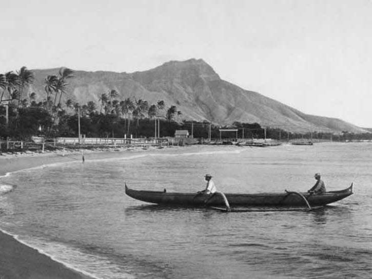 Circa 1900's, Two local men in their raft rest by the beach at Waikiki Bay, showing Diamond Head Getty Images