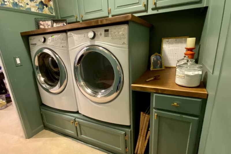 Green wainscoting, bold floral wallpaper on upper half of wall, countertop built on top of washer and dryer with built in cabinets above