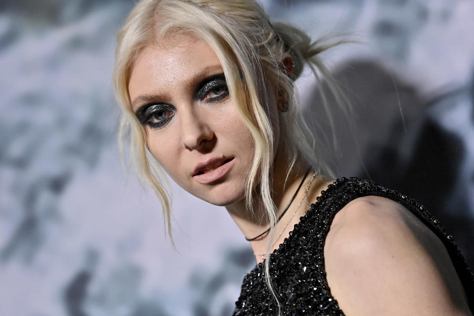 Head and shoulders shot of Taylor, her white blonde hair tied back with waves left free at the front. She has bold black glittery eyeshadow on and a black sequined sleeveless top.