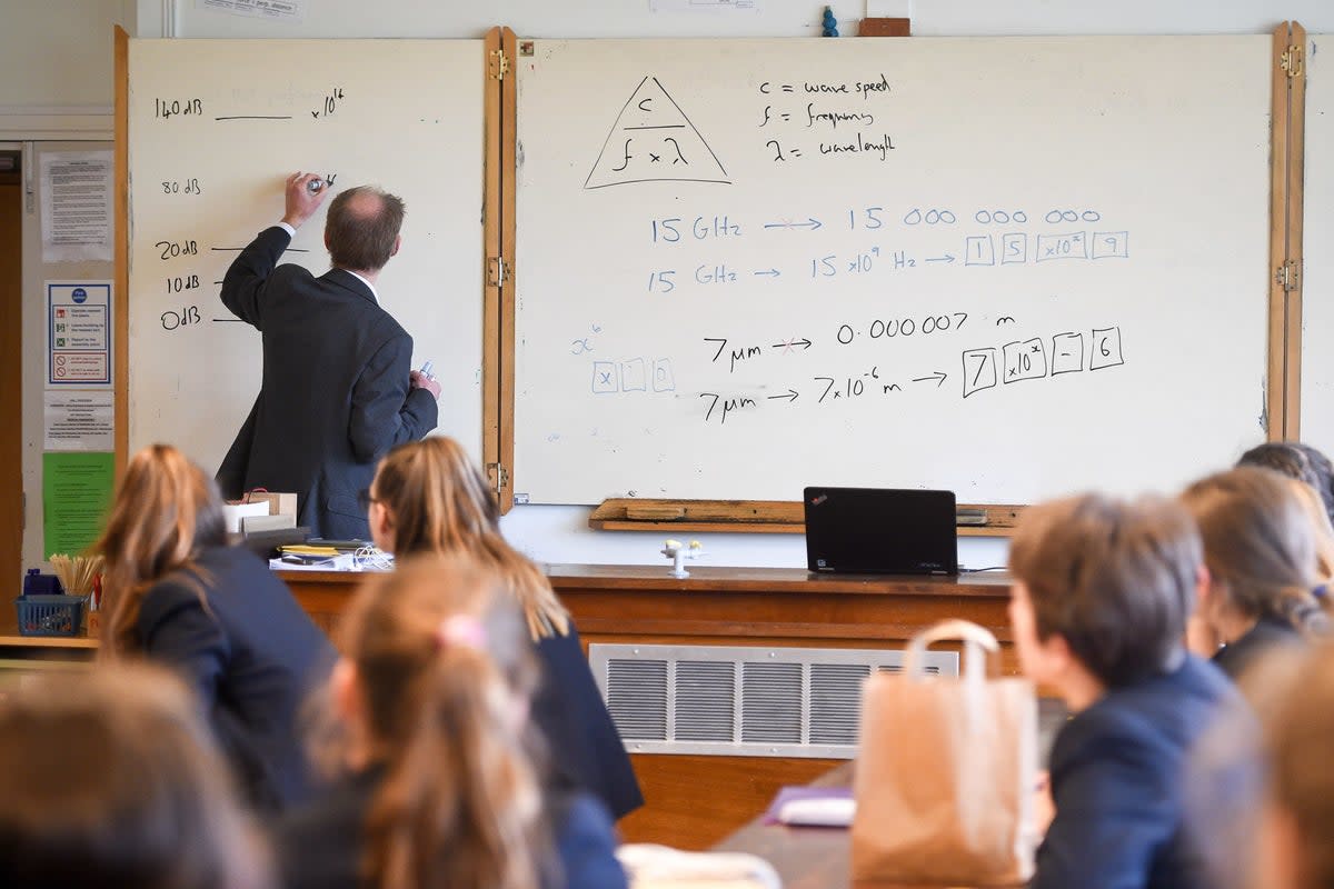 A teacher writes on a whiteboard (PA) (PA Archive)