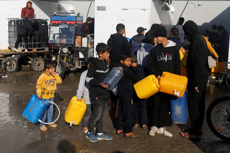 Palestinian children queue as they wait to collect drinking water, amid shortages of drinking water, as the conflict between Israel and Hamas continues, in Rafah