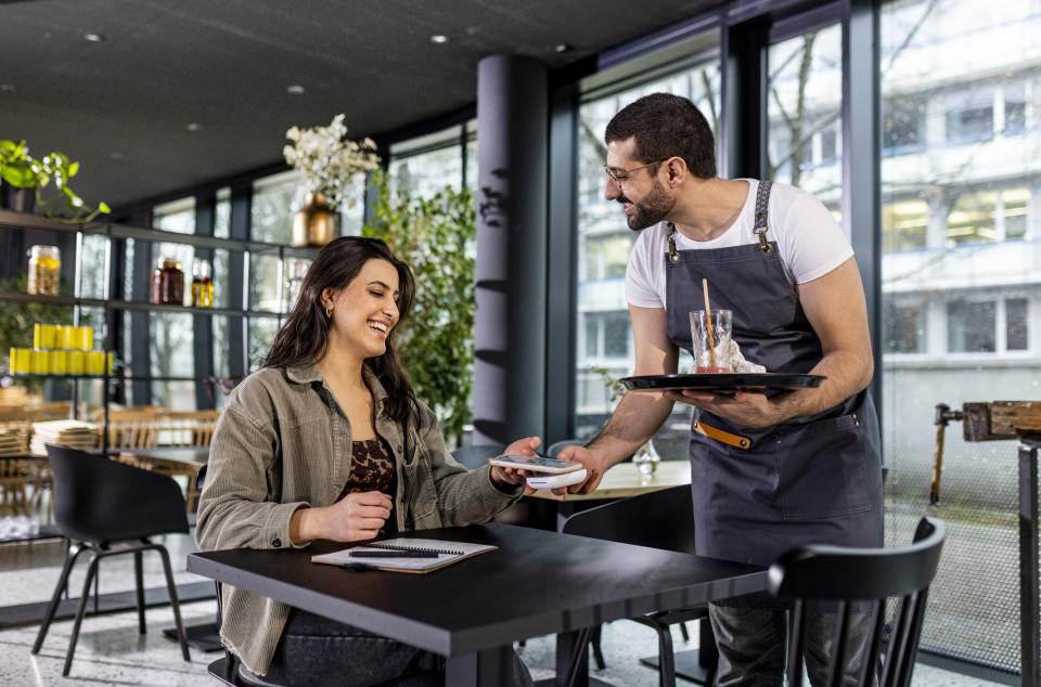 A smiling waitress takes an order from a woman sitting at a cafe table