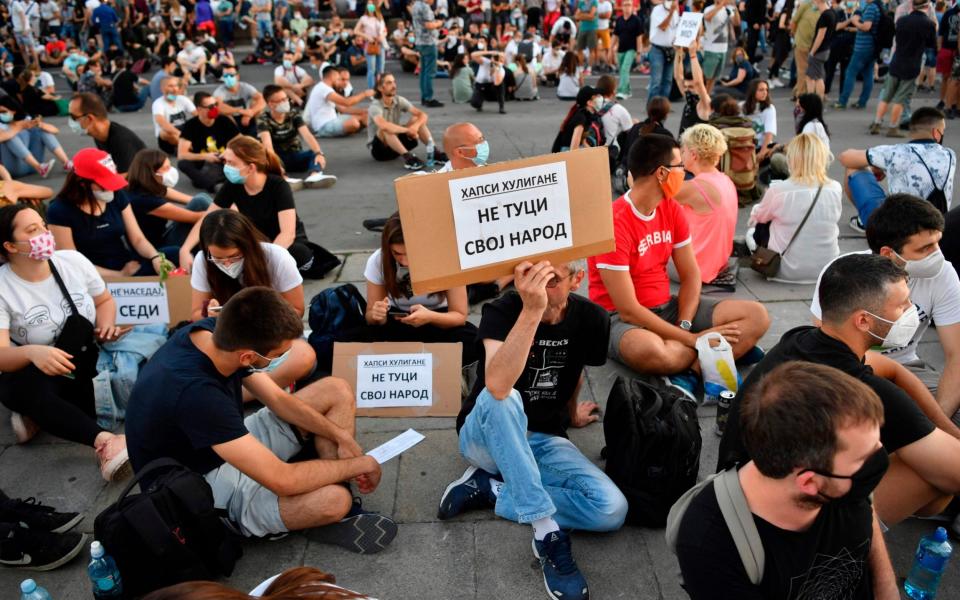 People sit holding placards reading "Don't beat your own people" or "Arrest hooligans" during the protest in Belgrade  - Andrej Isakovic/AFP