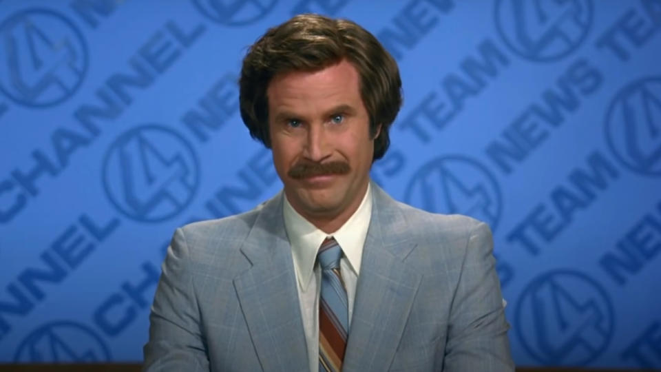 Will Ferrell smiles confidently at the news desk in Anchorman The Legend of Ron Burgundy.