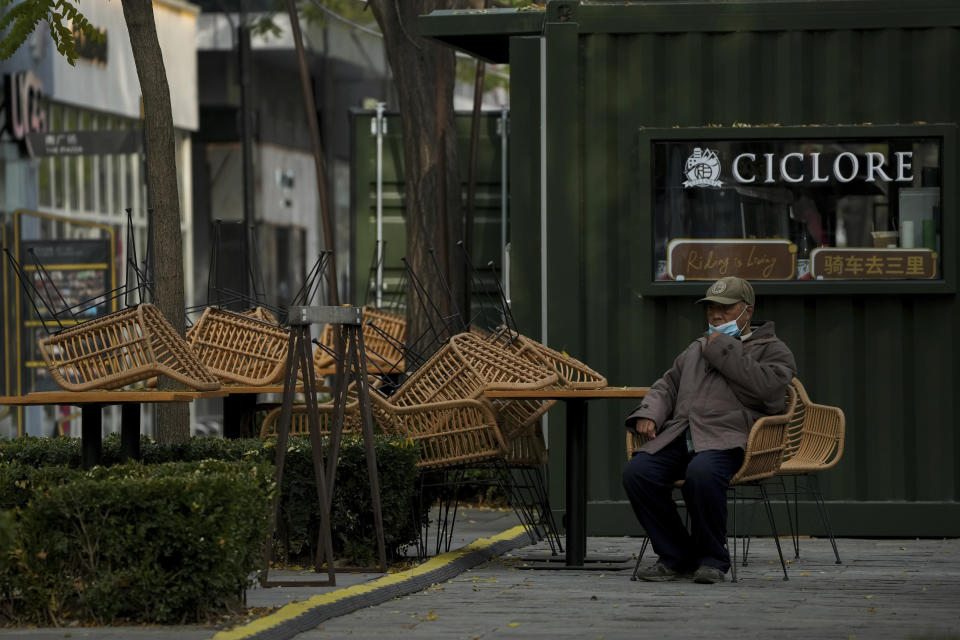 A resident puts on his face mask as he rests at a closure cafe and restaurant outside a shuttered shopping mall as part of COVID-19 controls in Beijing, Tuesday, Nov. 22, 2022. Anti-virus controls that are confining millions of Chinese families to their homes and shut shops and offices are spurring fears already weak global business and trade might suffer. (AP Photo/Andy Wong)