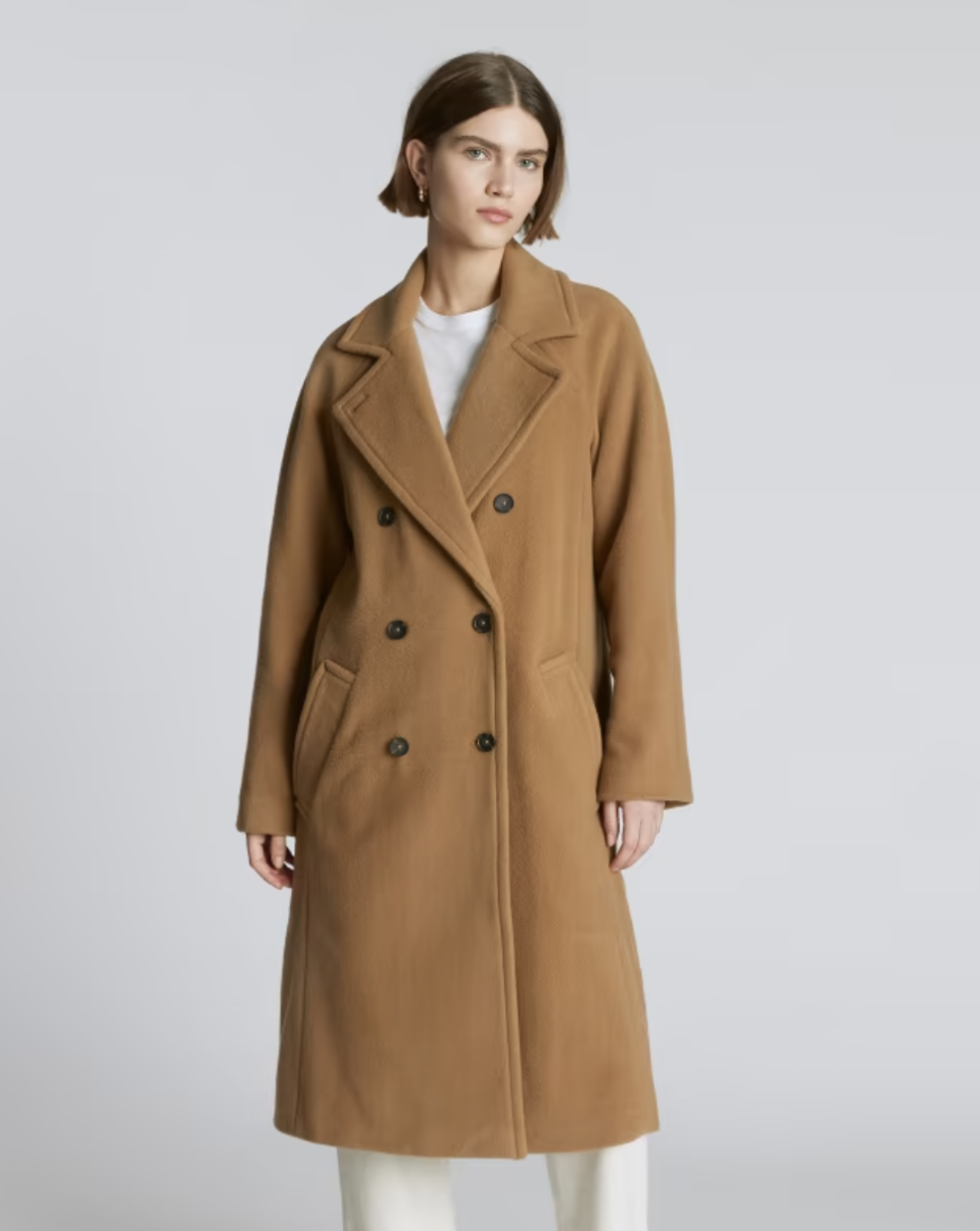 model wearing white pants and buttoned The Italian ReWool Long Peacoat in Camel (Photo via Everlane)