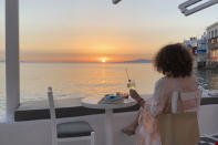 In this Tuesday, June 9, 2020 photo, a visitor watches the sunset at a bar in an area known as Little Venice in the main town of the island of Mykonos, Greece. Business owners and locals officials on the Greek holiday island of Mykonos, a popular vacation spot for celebrities, club-goers, and high rollers, say they are keen to reopen for business despite the risks of COVID-19 posed by international travel. Greece will official launch its tourism season Monday, June 15, 2020 after keeping the country's infection rate low. (AP Photo/Derek Gatopoulos)