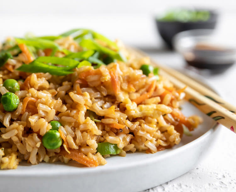 Healthy fried rice is shown in this photograph on a while plate with chopsticks. 