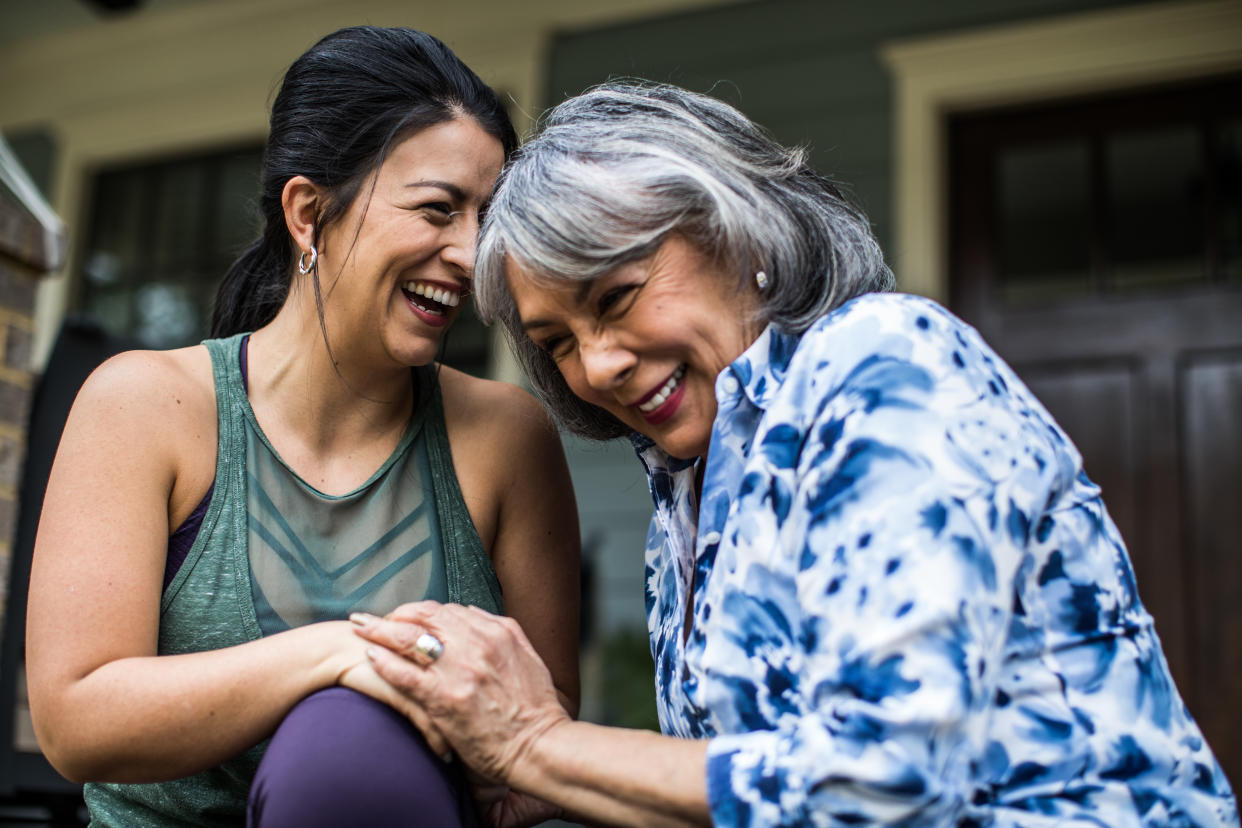 Happy senior woman and adult daughter laughing on porch.