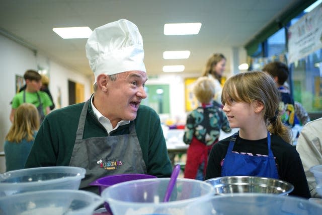 Sir Ed Davey, wearing a chef's hat for a cookery lesson, speaks to a child at a school in Harpenden, Hertfordshire