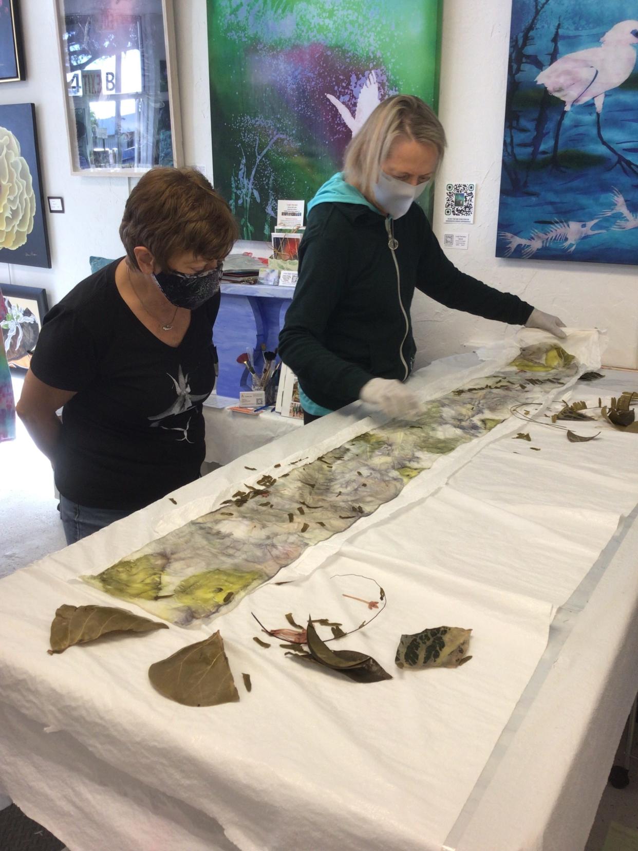 Artist Leigh Herndon watches as student christin Pryor unrolls a botanical transfer shibori panel; Herndon offers classes, with information on her website, leighdesignsnaples.com.