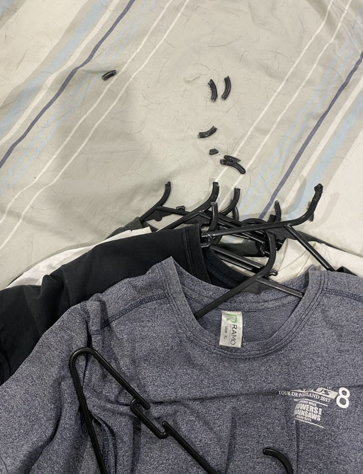Pile of clothing hanging on multiple black plastic hangers with the tops chewed off