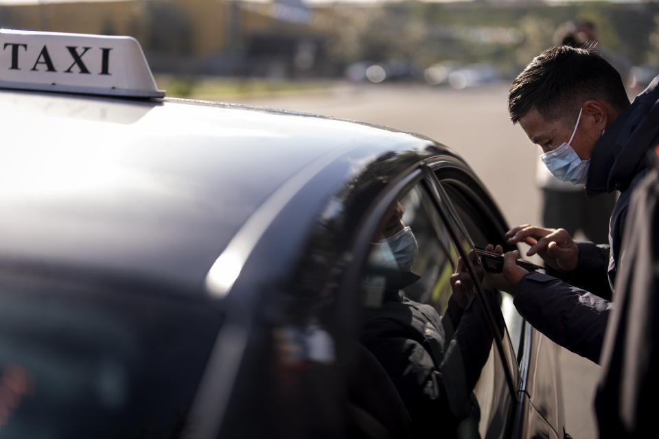 A migrant speaks to a taxi driver using a translation application on his phone as he arrives at a bus stop after leaving a processing facility, Friday, Feb. 23, 2024, in San Diego. Hundreds of migrants were dropped off Friday at a sidewalk bus stop amid office parks in San Diego with notices to appear in immigration court after local government funding for a reception center ran out of money sooner than expected. (AP Photo/Gregory Bull)