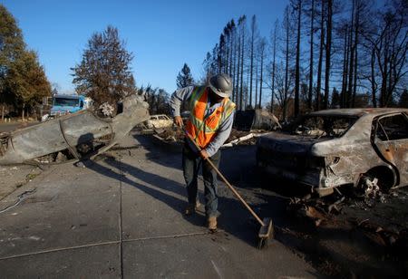 An employee of Pacific Gas & Electric (PG&E) sweeps the sidewalk in a destroyed neighborhood after a wildfire tore through Santa Rosa, California, U.S., October 15, 2017. REUTERS/Jim Urquhart