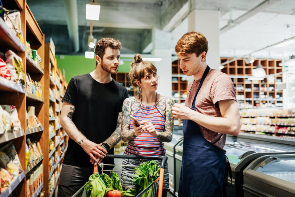 A supermarket clerk assisting a young couple with tattoos while they are out grocery shopping together.