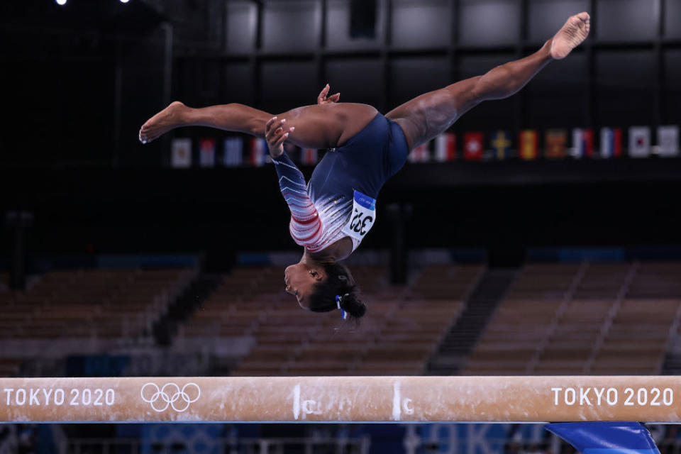 Simone upside down as she's mid-air over the balance beam