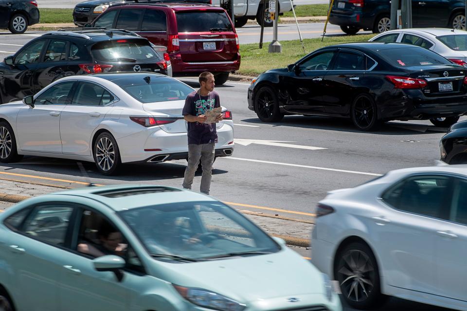Sean Alcock, who is homeless, stands in the middle of Patton Ave. asking for help from motorists August 4, 2023.