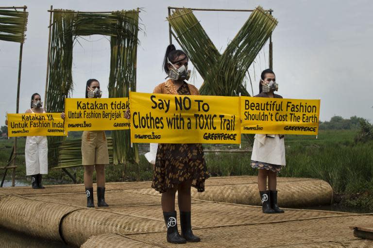 Indonesian models with gas masks wearing dresses by Lenny Agustin, Felicia Budi and Hana Farhana display banners during a fashion show in a polluted river basin in western Java island, March 22, 2015