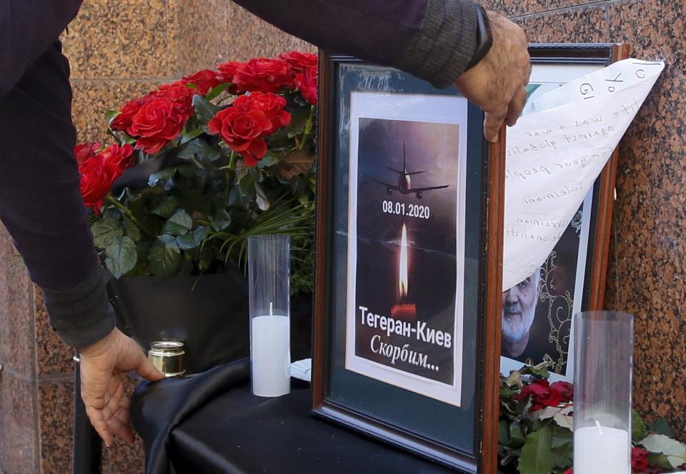 A man places a memorial poster showing a Ukrainian 737-800 plane that crashed on the outskirts of Tehran, Iran, and and a candle, the words reading "Tehran - Kyiv, we're mourning" outside the Iranian Embassy in Kyiv, Ukraine, Wednesday, Jan. 8, 2020. A Ukrainian airplane carrying 176 people crashed on Wednesday shortly after takeoff from Tehran's main airport, killing all onboard, Iranian state TV and officials in Ukraine said. The portrait of Iranian Revolutionary Guard Gen. Qassem Soleimani killed by U.S. airstrike in Iraq is seen behind. (AP Photo/Efrem Lukatsky)