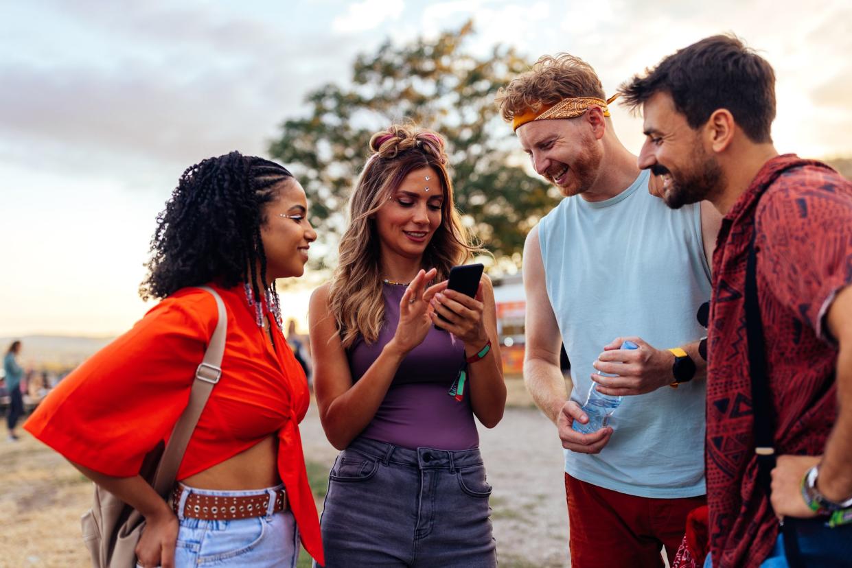 A young group of friends are at summer festival, looking up a line up of dj's at the main stage.